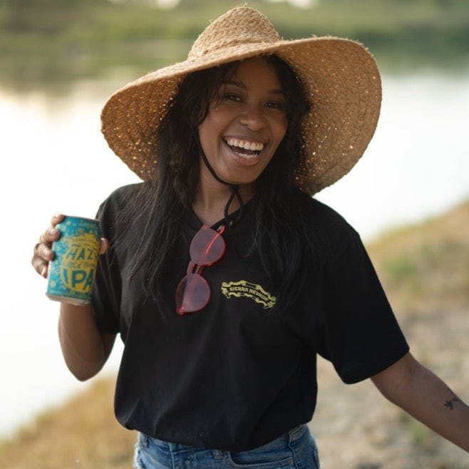 Sierra Nevada Hazy Little Thing black t-shirt, worn by a woman enjoying a Hazy Little Thing IPA on the side of a river.