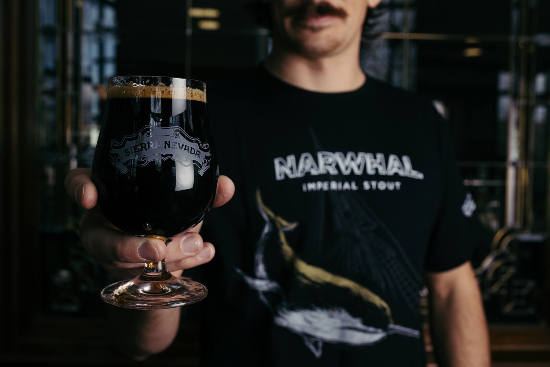 A young man holds out a glass of Sierra Nevada Narwhal Imperial Stout