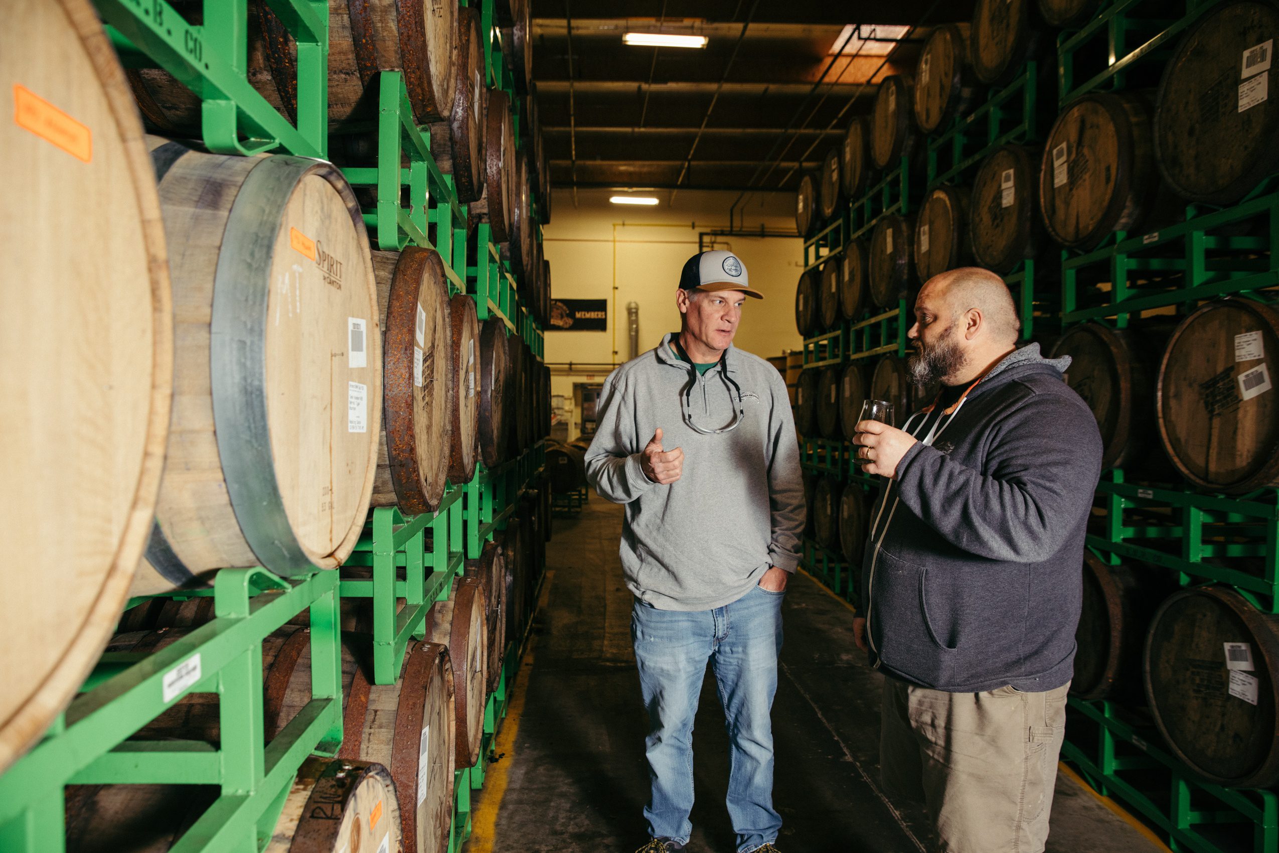 Two Sierra Nevada brewers talking next to stacks of wooden barrels