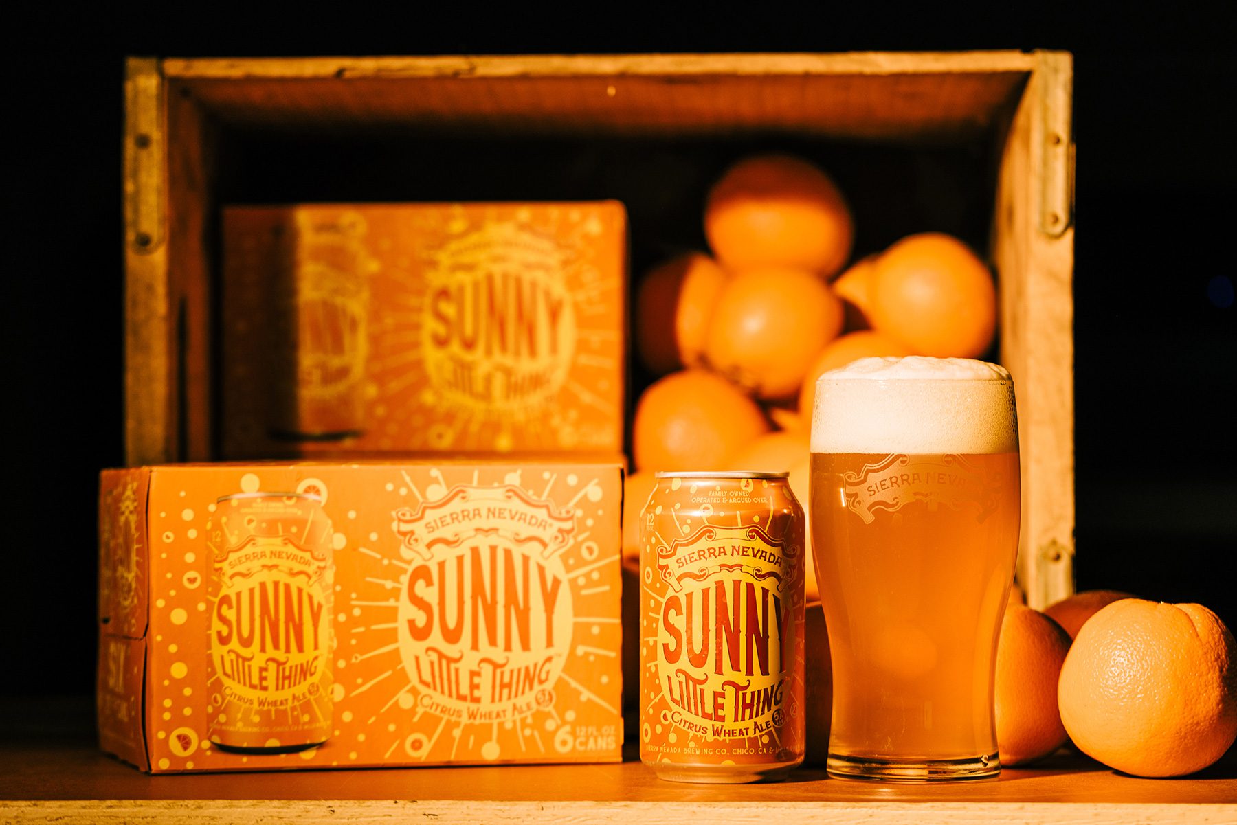 A can and full glass of Sunny Little Thing in front of a crate of oranges