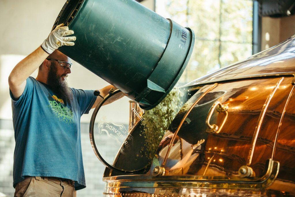 A Sierra Nevada brewer adding hops to a brew kettle