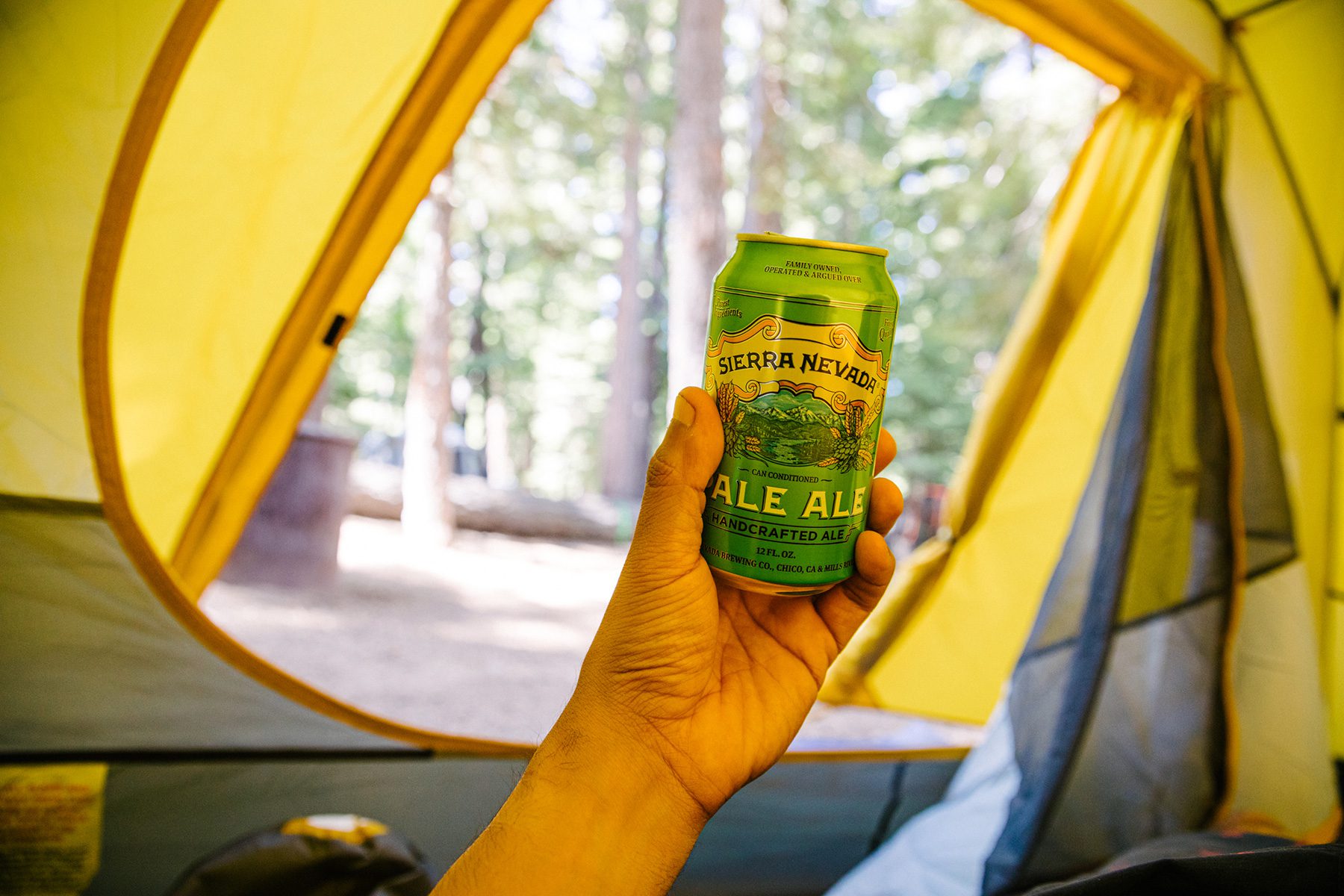 A hand holding a can of Sierra Nevada Pale Ale, looking out from a camping tent