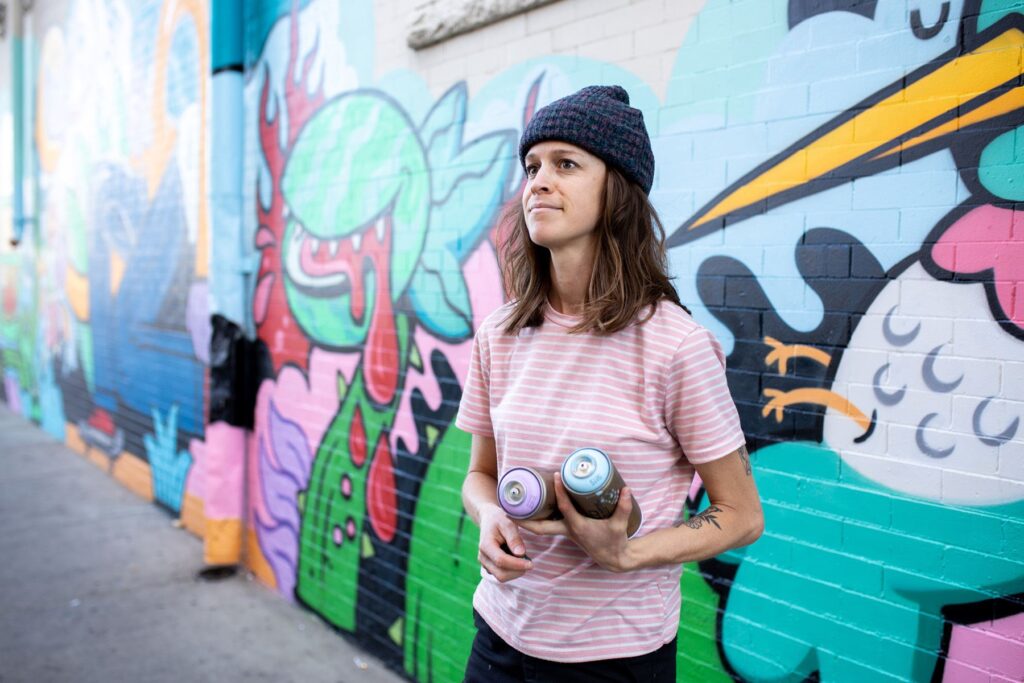 Artist Hannah Eddy holding two cans of spray paint