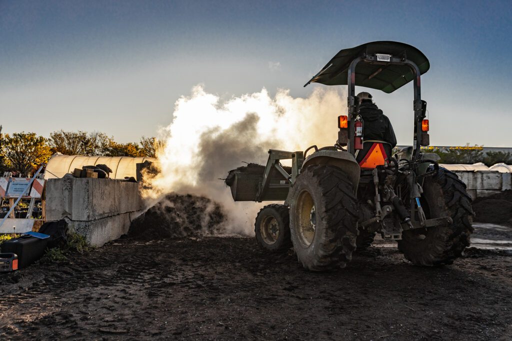 A tractor moving compost piles that are steaming in the cool morning air