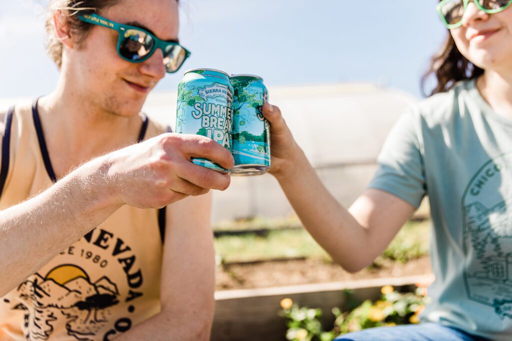 Young guy and young woman raising cans of Summer Break IPA in a cheers