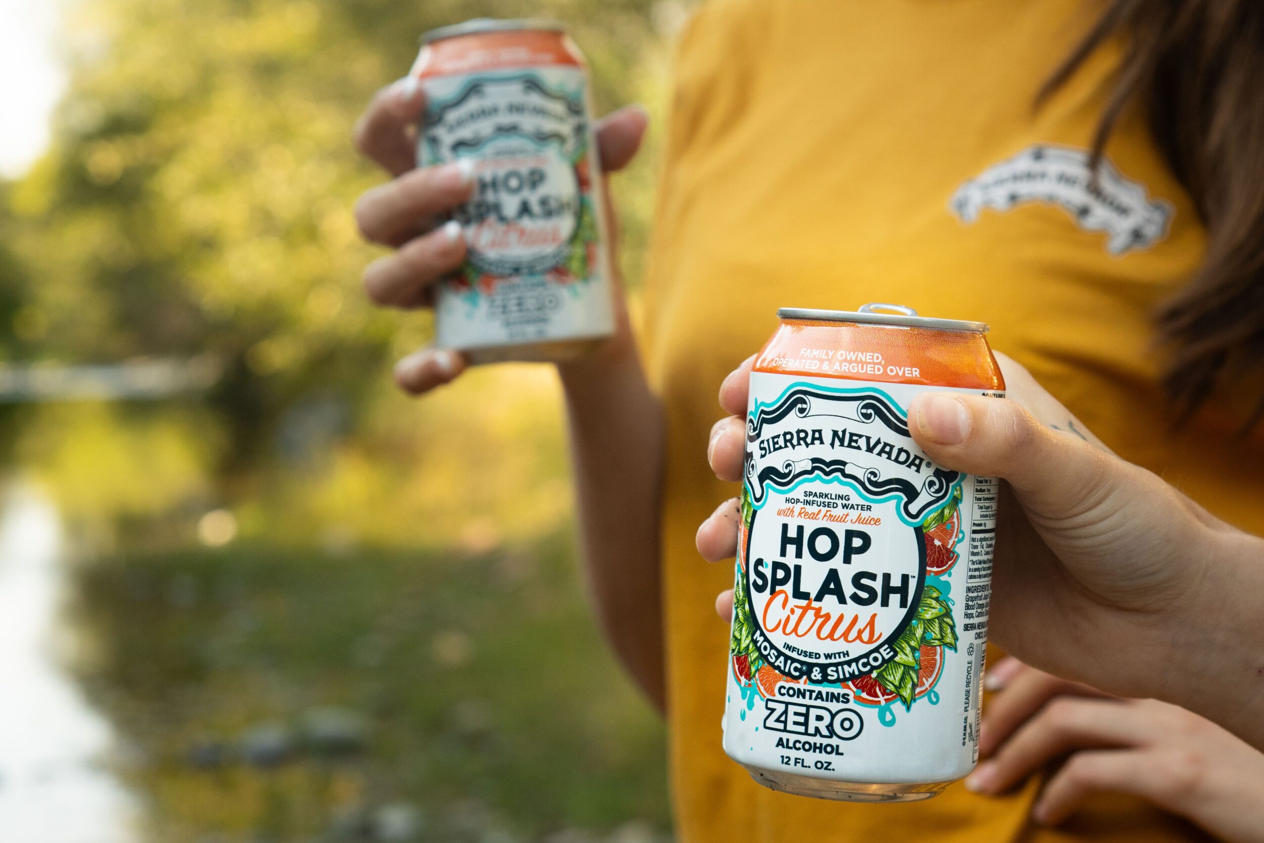 Two people, next to a creek, holding cans of Sierra Nevada Hop Splash Citrus