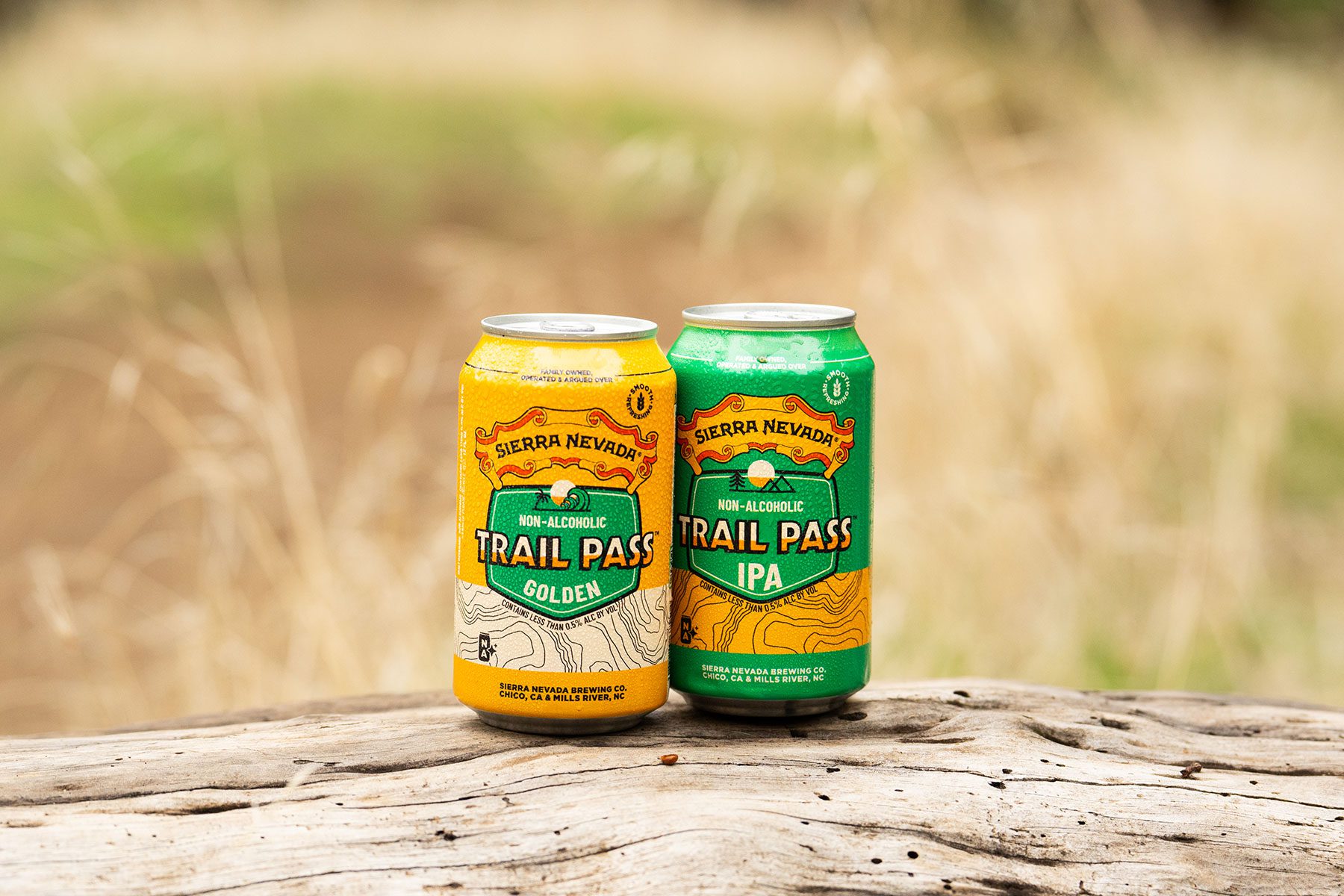 A can of non-alcoholic Sierra Nevada Trail Pass Golden and a can of Trail Pass IPA sitting on a log