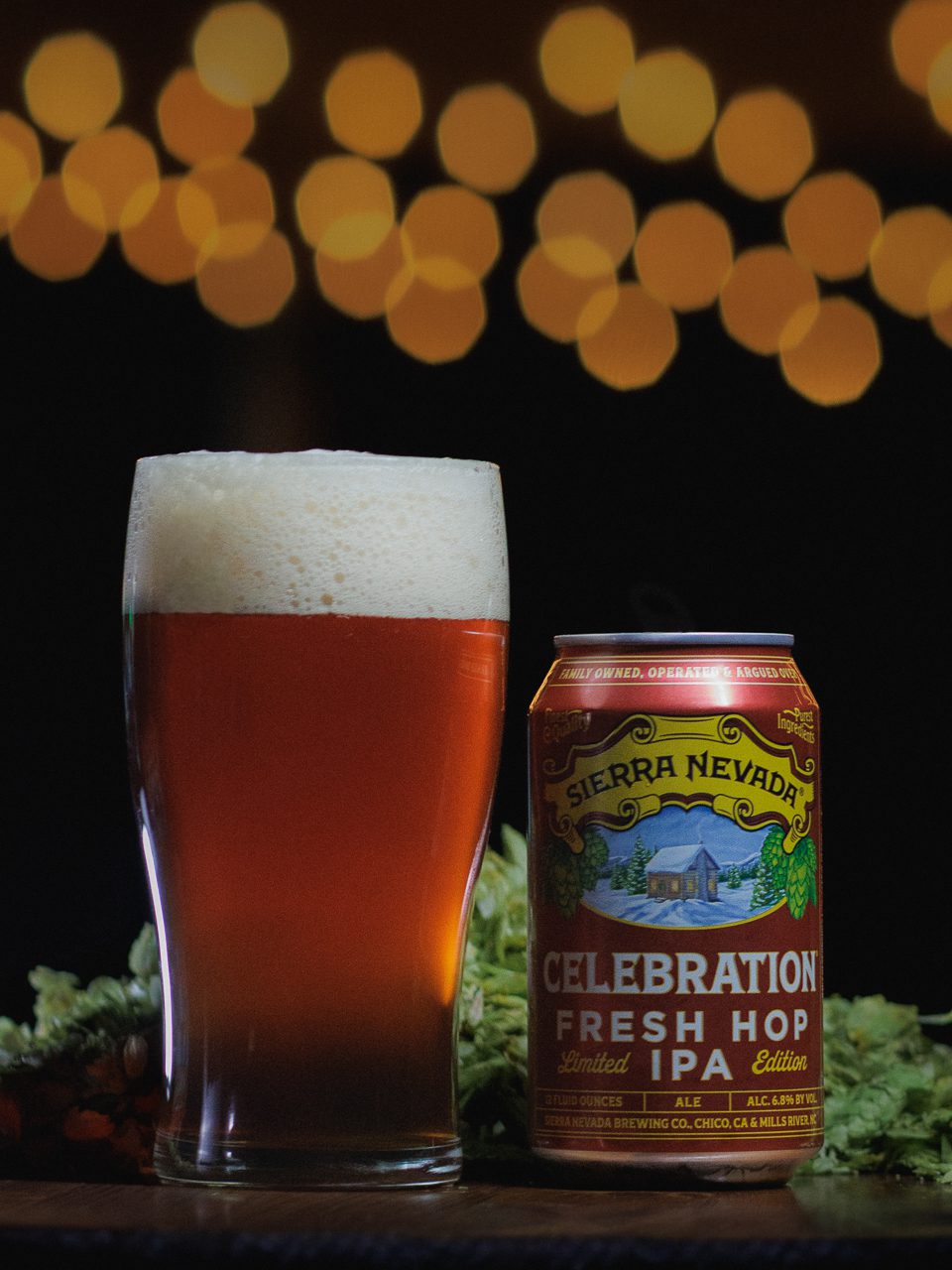 A full glass and can of Celebration Fresh Hop IPA surrounded by hops